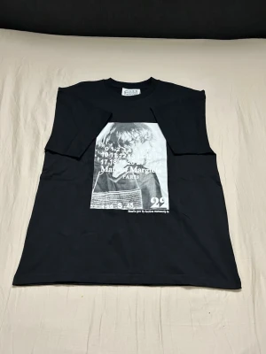 Svart t-shirt Maison Margiela print - Cool svart t-shirt från Maison Margiela med stort grafiskt print framtill i vitt och grått. Klassisk rund hals och normal passform. Tillverkad i mjuk bomull som känns skön mot huden. Perfekt för dig som gillar statement-plagg och streetstyle.