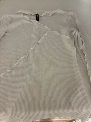 Vit ribbad topp från Divided H&M - Säljer en vit långärmad topp från Divided H&M med ribbad struktur och vågiga kanter vid hals, ärmslut och nederkant. Materialet är mjukt och stretchigt, perfekt till fester men även vardagsklädsel! Priset går o diskutera☺️