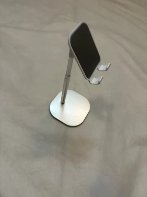 Justerbart mobilställ i silver - Snyggt och modernt mobilställ i silverfärgad metall med svart yta där mobilen vilar. Stället har justerbar höjd och vinkel, perfekt för skrivbordet. Passar de flesta smartphones och ger stabilt stöd när du kollar på videos eller pluggar.