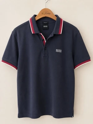 Marinblå piké från Hugo Boss (L) - Snygg marinblå pikétröja från Hugo Boss med vita och röda detaljer på krage och ärmslut. Klassisk passform med korta ärmar och knappar framtill. Boss-logga broderad på bröstet. Perfekt till jeans eller shorts.
