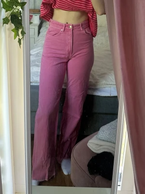 Rosa high waist jeans med raka ben - Säljer ett par snygga rosa jeans med high waist och raka ben. Jeansen har klassisk femficksmodell, gylf med dragkedja och knapp samt bälteshällor. Materialet är denim i bomull och färgen är en cool rosa ton. Perfekta för dig som vill sticka ut lite extra! Jag är 180cm.