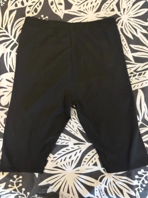 Svarta ribbade cykelshorts - Säljer ett par svarta cykelshorts med ribbad struktur. De har en midjehög passform och är perfekta för en sportig look. Materialet känns stretchigt och bekvämt, vilket gör dem smidiga att röra sig i. Passar till många olika stilar och outfits.