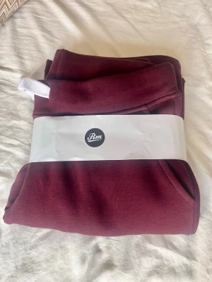 Burgundy mjukisbyxor Russemerch M - Snygga burgundy mjukisbyxor från Russmerch i storlek M. Tillverkade i mjukt material med resår i midjan och vita dragsnören. Perfekta för chill dagar och har en klassisk passform. Ekologisk bomull enligt märkning på tag. Ny med prislapp då jag fick dessa i födelsedagspresent men de passade tyvärr inte! Nypris 500