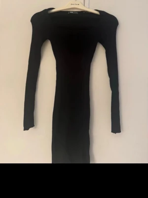 Svart långärmad klänning FB Sister - En svart, tight långärmad klänning från FB Sister. Klänningen har en enkel och stilren design med rund halsringning och figurnära passform. Perfekt för dig som gillar minimalistisk stil och vill ha en klassisk bas i garderoben.