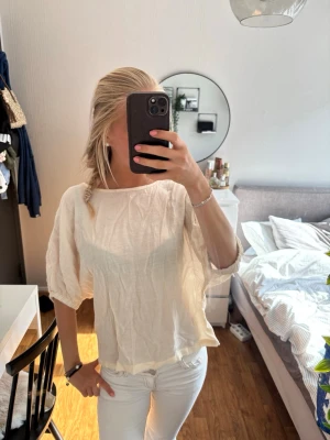 Ljusvit blus med puffärm - Säljer en ljusvit blus med trekvarts puffärmar och lös passform. Toppen har en enkel, stilren design och är tillverkad i ett tunt, luftigt material som känns skönt mot huden. Perfekt att matcha med jeans eller kjol för en fräsch look.