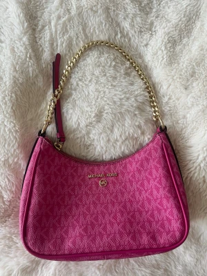 Rosa Michael Kors handväska - Säljer en snygg rosa handväska från Michael Kors med guldfärgad kedjerem och diskret MK-mönster över hela väskan. Väskan har en bågformad siluett och detaljer i guld, samt dragkedja upptill. Perfekt accessoar för att lyfta din outfit.