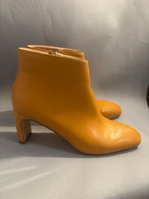 Helt Ny Na-KD Snygga stövletter med medelhög klack och dragkedja på sidan.Gula läderstövletter med klack - Helt Ny Na-KD Snygga stövletter med medelhög klack och dragkedja på sidan. Skorna har en stilren, minimalistisk design med rundad tå och markerade sömmar framtill. Perfekta för dig som vill sticka ut med färg och gillar trendiga boots.                                         OBS! det finns små märken Se sista bilden.  