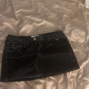 Svart jeanskjol från D&G - Snygg svart jeanskjol från D&G med klassisk femficksdesign och knappgylf. Perfekt för en trendig look. Den har en kort längd och är tillverkad i slitstarkt denimtyg. Ny pris 600 säljer för 250 