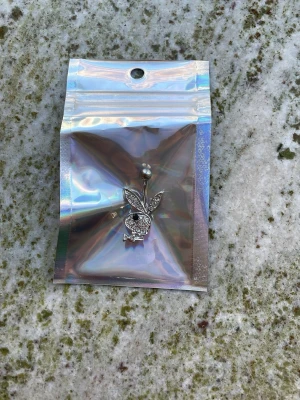 Playboy navelpiercing i silver - Säljer en snygg playboybunny navelpiercing i silverfärg och glittrande stenar. Piercingen har en klassisk stålkula och kaninen är täckt av små kristaller. Aldrig använd.