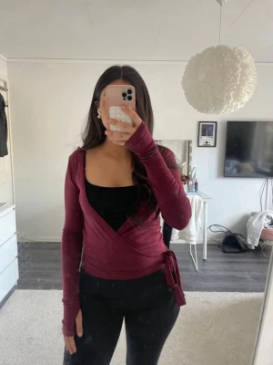 Vinröd omlotopp med knyt - Vinröd omlottopp med långa ärmar och knyt i sidan. Säljer då den aldrig kommit till användning. Perfekt att styla med ett linne under.