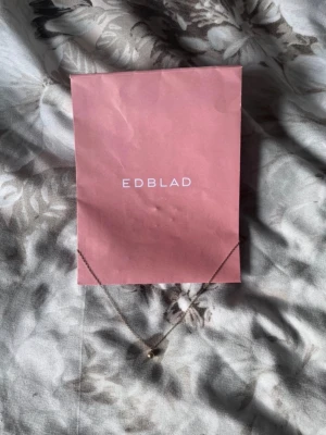 Guldhalsband med pärldetalj från Edblad - Snyggt och stilrent halsband från Edblad i guldtonad metall med en liten rund pärldetalj som hänge. Kedjan är tunn och har ett diskret lås med förlängningskedja. Perfekt för dig som gillar minimalistiska smycken med en elegant touch.