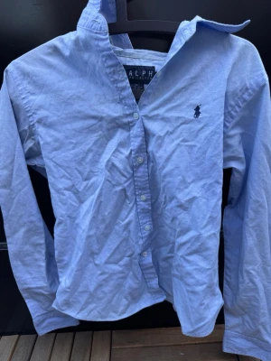 Ljusblå linne skjorta från Ralph Lauren🤩🙌 - Klassisk ljusblå skjorta från Ralph Lauren med knappstängning och broderad logga på bröstet. Skjortan har lång ärm och normal passform, perfekt till jeans eller chinos. Tillverkad i mjuk bomull för en bekväm känsla.🙌🤩