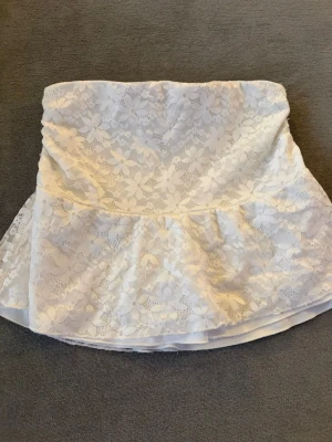 Vit spetskjol med volang - Supersöt vit kortkjol med blommigt spetsmönster och volangkant. Kjolen har en feminin och romantisk look, perfekt för dig som gillar en ljus och somrig stil. Ingen synlig dragkedja eller knappar.