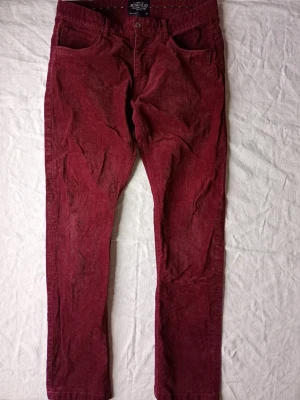 Vinröda manchesterbyxor från Point - Säljer ett par vinröda manchesterbyxor från Point med klassisk femficksmodell och raka ben. Byxorna har en snygg struktur i manchestertyg och knappgylf. Perfekta för dig som vill ha en retro och trendig look.