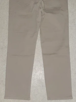 Beiga chinos från Emporio Armani - Snygga beiga chinos från Emporio Armani med klassisk rak passform. Byxorna har diskreta bakfickor och det ikoniska Armani-logotypen ovanför fickan. Tillverkade i ett mjukt och slitstarkt bomullsmaterial som känns bekvämt hela dagen.