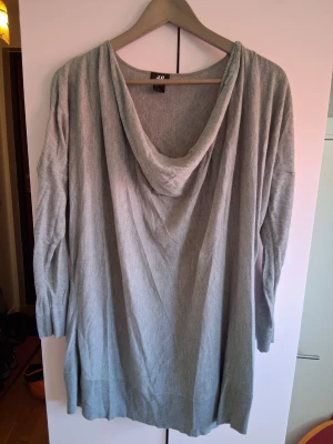 Ljusgrå stickad tröja från H&M - Mysig ljusgrå stickad tröja från H&M med lös passform och draperad krage. Tröjan har långa ärmar och ribbade muddar vid ärmslut och nederkant. Perfekt för lager på lager och chill stil.