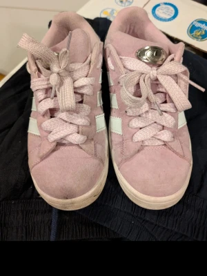 Adidas Campus rosa sneakers i mocka - Säljer ett par Adidas Campus sneakers i ljusrosa mocka med vita ränder och detaljer. Skorna har klassisk snörning, platt sula och svart detalj på hälen. Perfekta för dig som gillar retrostil och vill sticka ut med färg.