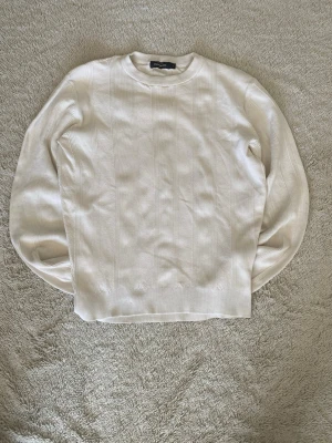 Vit stickad tröja från Dressman - Klassisk vit stickad tröja från Dressman med diskret ribbat mönster. Tröjan har rund halsringning, långa ärmar och ribbade muddar vid ärmslut och nederkant. Perfekt för en clean och stilren look.