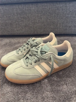 Adidas Samba ljusgröna sneakers - Nypris 1600, helt nya ej använda. Snygga Adidas Samba sneakers i ljusgrönt mocka med klassiska vita stripes och gummisula. Skon har en låg profil och beige detaljer på häl och plös. Perfekt för dig som gillar retrostil och streetwear.