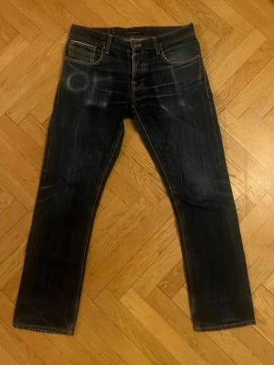 Nudie dry selvage - Säljer dessa Nudies i den populära modellen Grim Tim. Jeansen är dry selvage som är kända för att få riktigt fina slitningar med användning! Enda negativa är att det är små hål i fickorna, men går att laga gratis hos Nudie själva. Skriv om ni har frågor!  Mått  Midja:44cm Ytterbenslängd:103cm