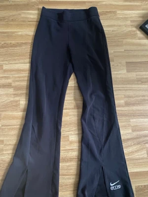 Svarta Nike Air leggings med slits - Snygga svarta leggings från Nike Air med broderad logga vid benslutet. Modellen har utsvängda ben och slits framtill. Mjukt och stretchigt material för maximal komfort. Använda en gång.