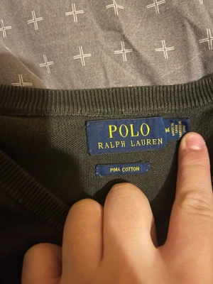 Mörkgrön tröja från Polo Ralph Lauren - Snygg mörkgrön tröja från Polo Ralph Lauren i mjuk Pima cotton. Tröjan har V-ringning, långa ärmar och ribbade muddar vid ärmslut och nederkant. Perfekt för dig som gillar klassisk och stilren design.