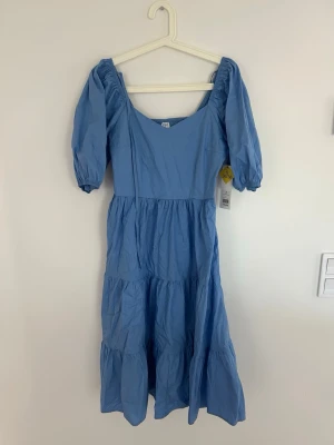 Blå puffärmad klänning S 36/38 - blå klänning med puffärmar och rundad urringning. Klänningen har en volangkantad kjol. Perfekt för sommarens alla tillfällen och ger en romantisk vibe.