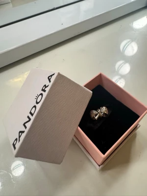 Pandora silverberlock, rosett - Säljer mitt berlock då jag aldrig använder. Den har små gnistrande stenar på rosetten som ger en elegant touch. Perfekt accessoar för att lyfta din stil.