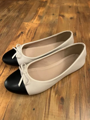 Beige ballerinaskor med svart tå - Stilrena ballerinaskor i beige med svart tå och liten rosett framtill. Skorna har rundad tå. Bra skick,  använda fåtal fånger, nån söm har gått upp bak på men inget jag märkt av (bild 4) storlek 40 men passar mig som oftast har 39/38. Perfekta till studenten eller sommaren! 