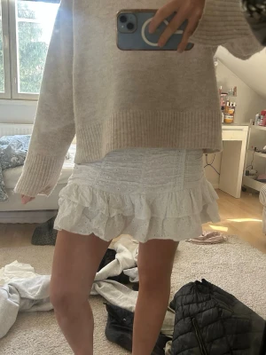 Vit volangkjol med broderade detaljer - Supersöt vit kortkjol med volanger och broderade detaljer. Kjolen har en smockad midja som ger en bekväm passform och ett luftigt fall. Perfekt för dig som vill ha en feminin och trendig look till sommaren.