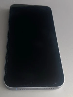 Ljusblå iPhone med dubbla kameror - Säljer en ljusblå iPhone med stilren design och platt ram. Telefonen har två stora kameralinser på baksidan och en svart rektangulär MagSafe-platta. Framsidan är helsvart med glas och baksidan är i glas och metall. Perfekt för dig som gillar modern och clean look.