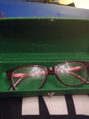 Röda glasögon från Specsavers - Snygga glasögon utan styrka från Specsavers med rektangulära bågar i mörkröd plast. Kommer i ett grönt fodral med Specsavers-logga. Perfekt accessoar för dig som vill ha en stilren och modern look.