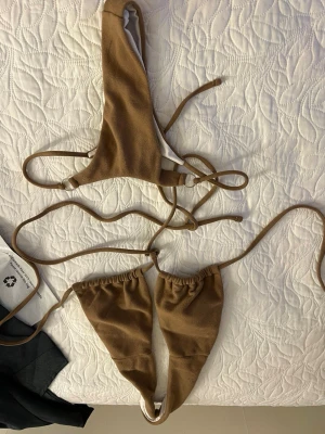 Brun bikini med snörning - Trendig brun bikini med trekantsöverdel och smala knytband. Underdelen har hög skärning och matchande snörning i sidorna. Materialet känns mjukt och stretchigt, perfekt för lata dagar på stranden.