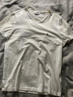 Vit v-ringad t-shirt från Dondup - Klassisk vit t-shirt från Dondup med v-ringning och liten broderad D-logga på bröstet. Tillverkad i mjuk bomull som känns skön mot huden. Perfekt basic-plagg för en clean och enkel stil.