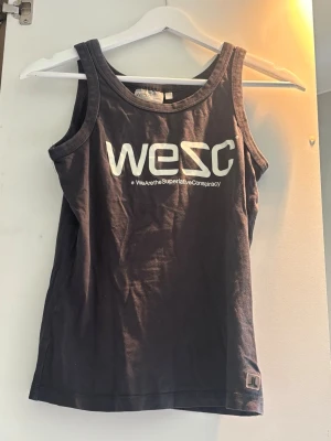 Svart linnetopp från WESC - Snygg svart linnetopp från WESC med vitt tryck framtill och logga. Klassisk rak modell med breda axelband och rundad halsringning. Perfekt till jeans eller shorts för en avslappnad stil.