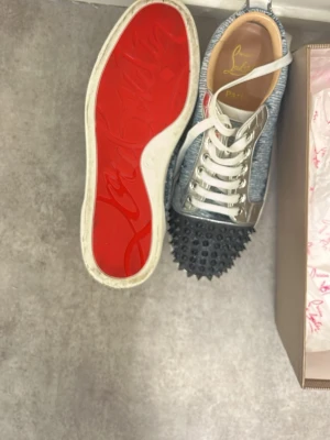 Christian Louboutin sneakers med nitar - Unika sneakers från Christian Louboutin med svartvita textilpaneler, silvriga detaljer och svarta nitar på tån. Skorna har vita snören och den klassiska röda sulan. Perfekt för dig som vill sticka ut med en edgy och exklusiv look. Använd 1-2 gånger kommer passa i allt. Pris går och diskutera jag har även tappat bort locket till lådan! Skriv om ni vill ha mer bilder