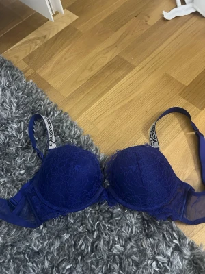 Blå spets-bh från Calvin Klein - Snygg blå bh från Calvin Klein med vadderade kupor och spetsdetaljer. Axelbanden har logotyptryck och bh:n har en klassisk bygelmodell. Insidan av kuporna är ljus och mjuk för extra komfort. Perfekt för dig som vill ha både stil och stöd.