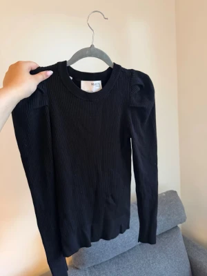 Svart  tröja med puffärm - Svart  tröja från Selected Femme med ribbad struktur och puffade axlar. Tröjan har rund halsringning och långa ärmar