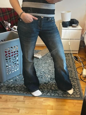 Blå bootcut jeans med fickdetaljer - Säljer ett par mörkblå bootcut jeans med snygga fickdetaljer bak och kontrastsömmar. Jeansen har låg midja och klassisk femficksdesign. Perfekta för dig som gillar en avslappnad men trendig look.