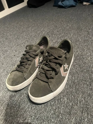 Grå Converse One Star sneakers - Snygga grå Converse One Star sneakers i mocka med vita och bruna detaljer på sidan samt den klassiska stjärnan. Skorna har lågt skaft, svarta skosnören och vit sula. Perfekta för dig som gillar streetwear och vill ha en stilren look. Storlek 40. Pris kan diskuteras vid snabb affär!