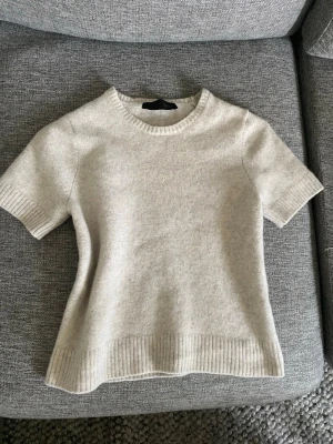 Beige stickad topp med kort ärm - Snygg beige stickad topp med korta ärmar och ribbade detaljer vid ärmslut, halsringning och nederkant. Toppen har en enkel och clean design som är lätt att matcha med olika stilar. Perfekt för dig som gillar en stilren och mysig look. Aldrig använd, orginalpris 499💕