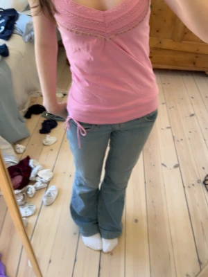 Rosa linnetopp från Cherokee - Söt rosa linnetopp från Cherokee med spetsdetaljer och smala axelband. Toppen har v-ringning och en dekorativ knytning i nederkanten. Perfekt för varma dagar och enkel att styla till jeans eller kjol.