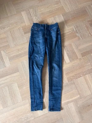 Levi's blå skinny jeans med hög midja - Säljer ett par klassiska blå skinny jeans från Levi's med hög midja och dubbla knappar i linningen. Jeansen har fem fickor, dragkedja och är tillverkade i stretchigt denimtyg för en bekväm passform. Perfekta till en avslappnad stil. Osäker på storlek men skulle säga S
