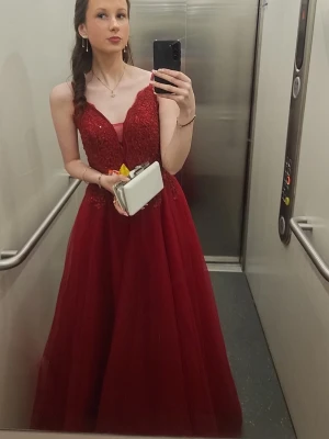 Röd långklänning med spetsdetaljer - Elegant röd långklänning med tunna axelband och v-ringad urringning. Överdelen har vackra spetsdetaljer och kjolen är i flera lager för en voluminös look. Perfekt för bal eller festliga tillfällen. Orginalstorlek: 36 men omsydd till en 34😊