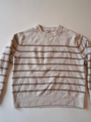 Beige stickad tröja med ränder - Säljer en beige stickad tröja med ljusbruna horisontella ränder. Tröjan har rund halsringning, långa ärmar och ribbade muddar vid ärmslut och nederkant. Perfekt för dig som gillar en enkel och stilren look.