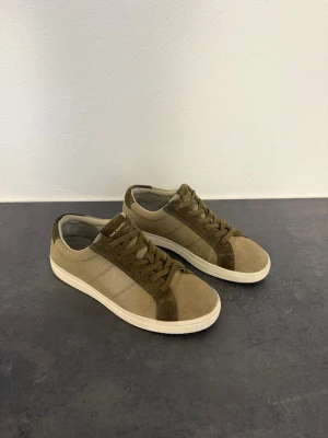 Gröna/Beige  sneakers från Boggi Milano, stl 43 - Snygga låga sneakers från Boggi Milano i  grön/ beige canvas med detaljer i mocka och vita sulor. Klassisk design med snörning och diskret logga på plösen. Perfekta för en avslappnad och stilren look.
