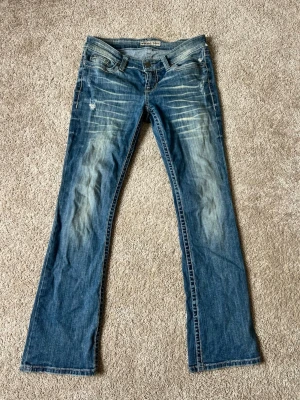 Blå bootcut jeans med slitningar - Snygga blå bootcut jeans med slitningar och ljusa tvättade partier framtill. Klassisk femficksmodell med låg midja och detaljerade sömmar. Perfekta för en avslappnad och trendig look. Tillverkade i bomullsdenim.