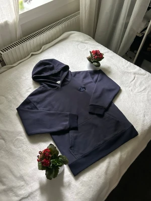Mörkblå CD hoodie  - Snygg mörkblå CD hoodie med stor magficka och huva. Hoodien har ribbade muddar vid ärmslut och nederkant samt en liten broderad detalj på bröstet. Perfekt för en avslappnad och stilren look. Tillverkad i mjukt bomullsmaterial.