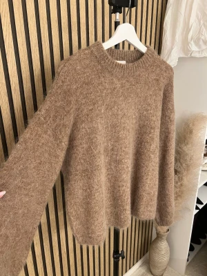 Brun fluffig stickad tröja i mohairmix  - Mysig brun stickad tröja med rund hals och oversized passform. Tröjan är fluffig och har långa ärmar samt ribbstickade muddar vid hals, ärmslut och nederkant. Perfekt för lager-på-lager och chill dagar.