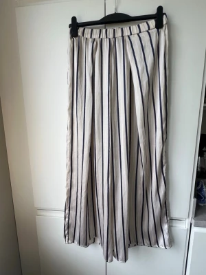 Randiga vida loungewear-byxor - Snygga och luftiga loungewear-byxor med vita och mörkblå vertikala ränder. Byxorna har breda ben och resår i midjan för extra komfort. Perfekta för chill dagar hemma eller när du vill ha en avslappnad stil. 